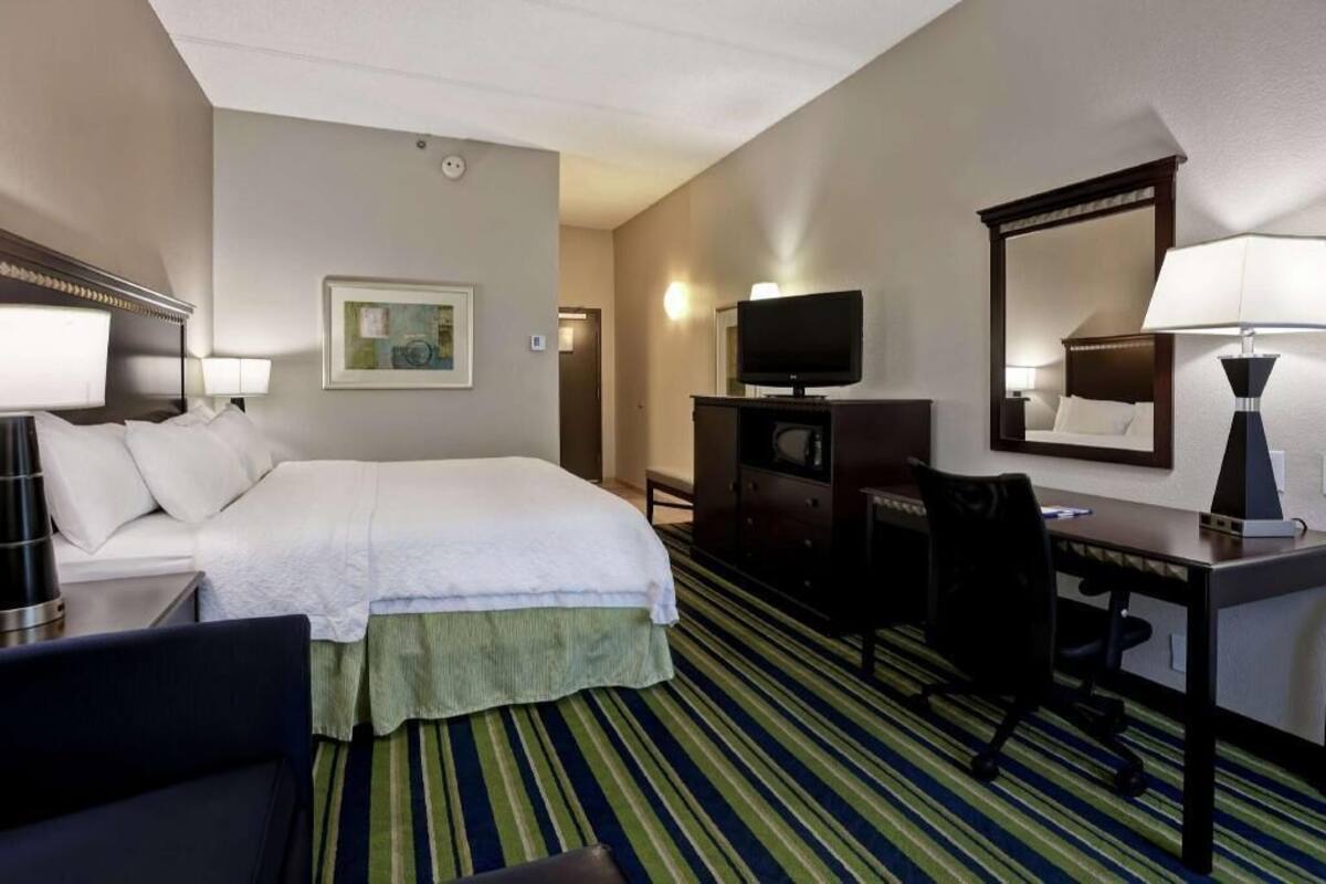 A hotel room with a bed, a desk, a chair, a television, and a mirror.