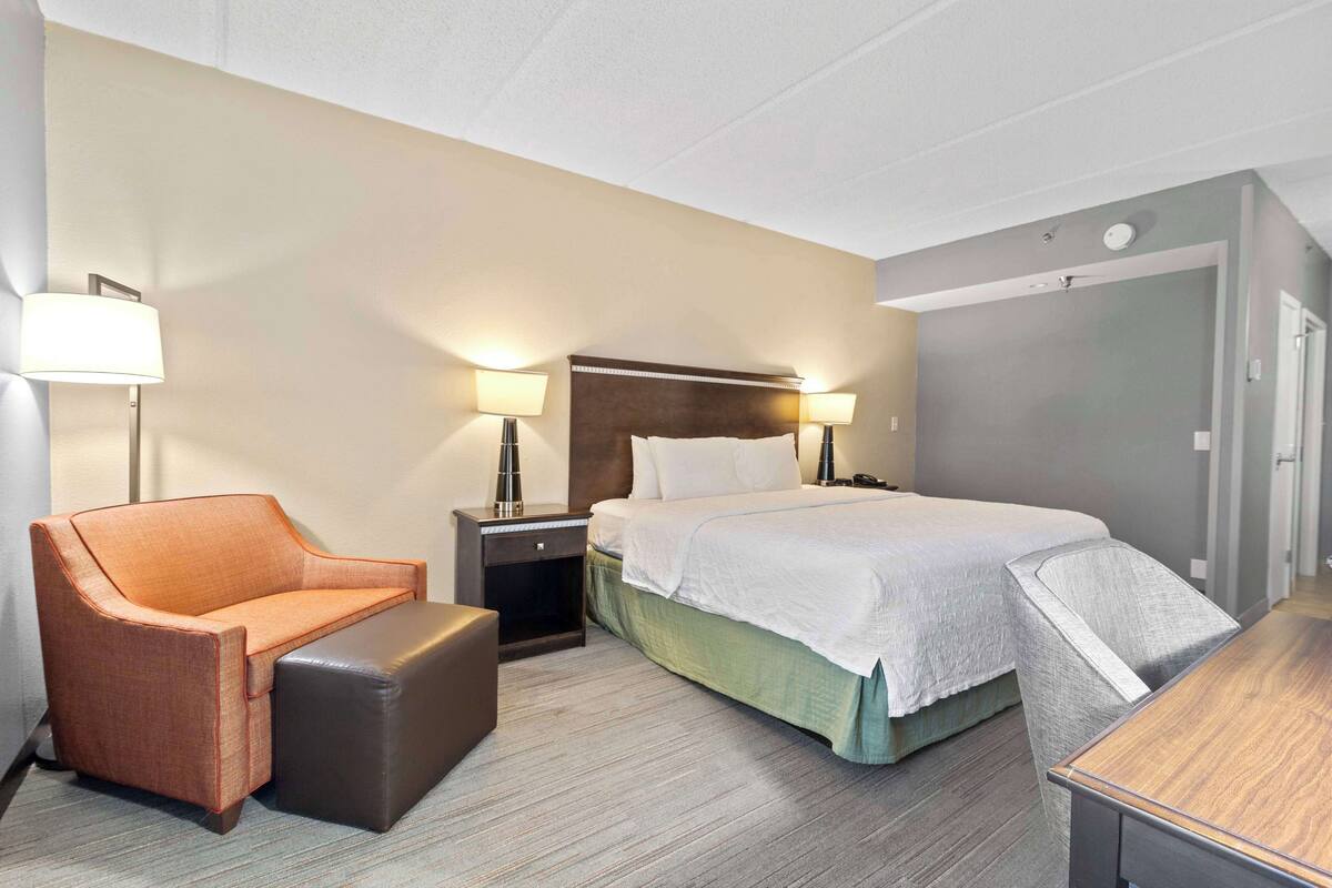 A hotel room with a bed, a chair, a small table, and two bedside lamps.