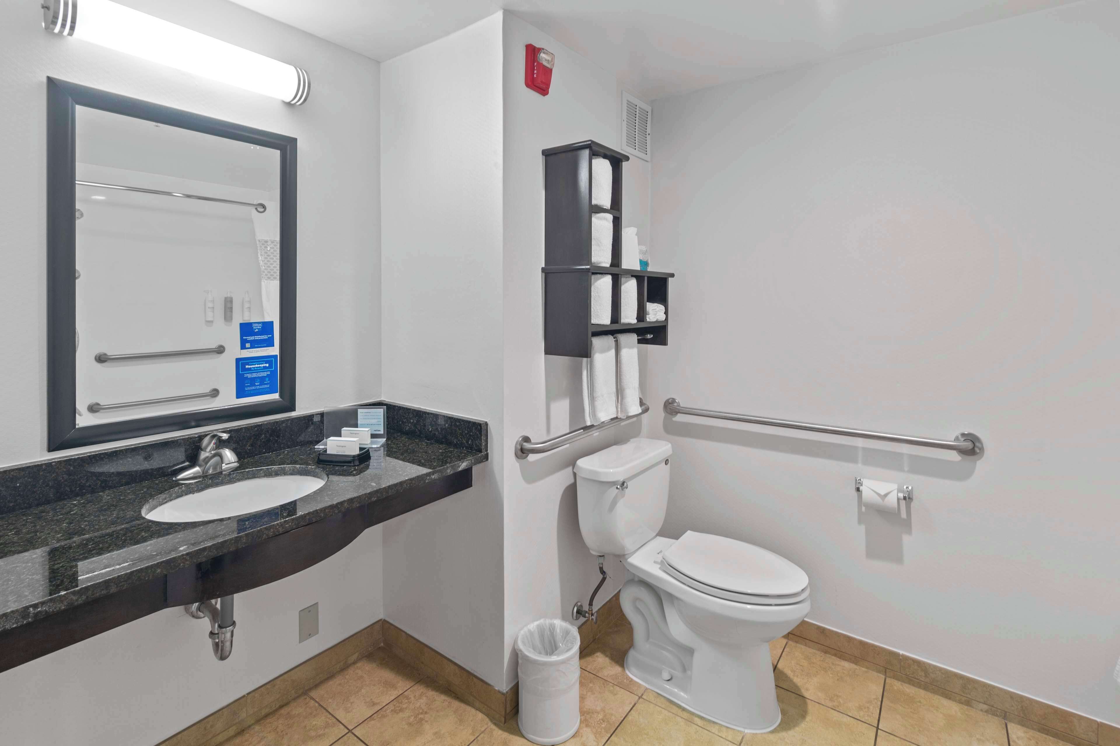 Un baño moderno con lavamanos, espejo, inodoro y barras de apoyo.