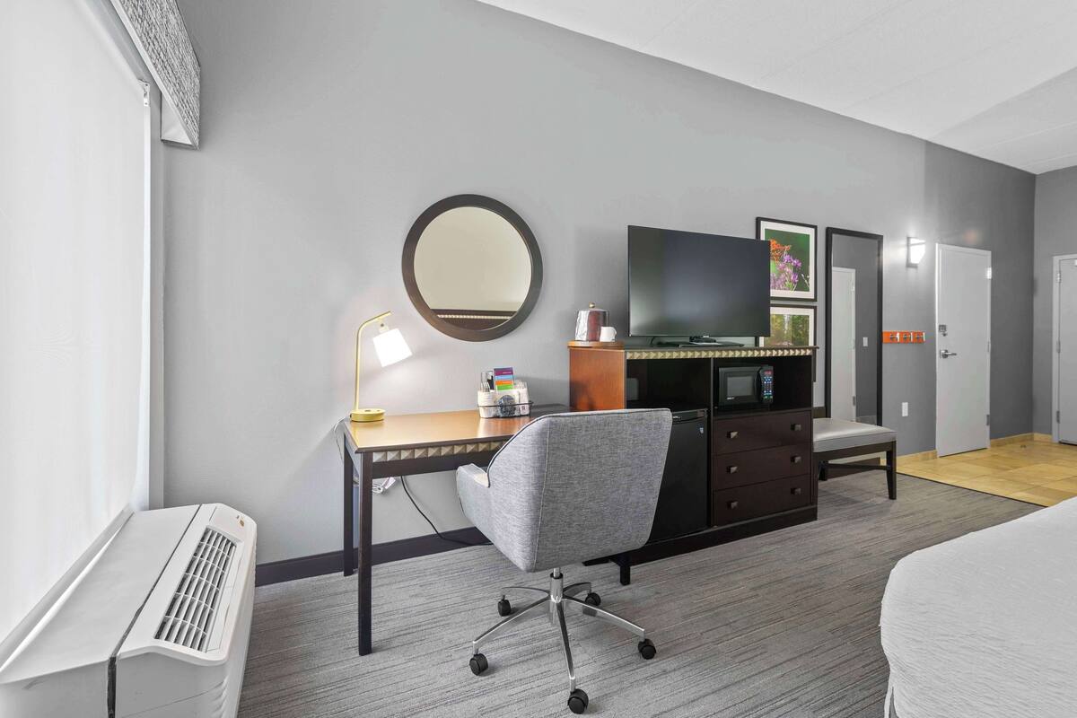 A hotel room with a desk, chair, television, wardrobe, and a bed.