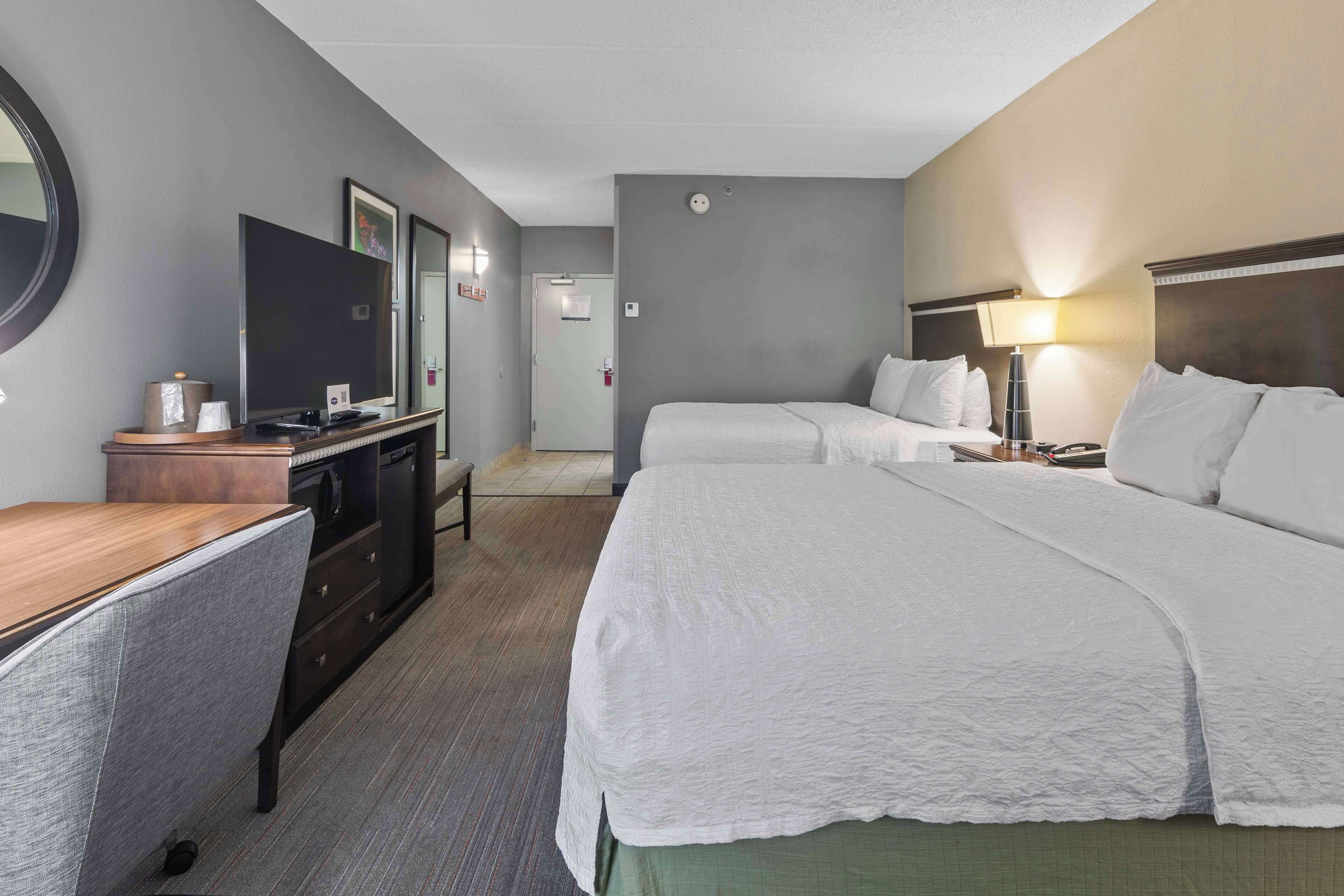 A hotel room with two beds, a desk, a TV, and a mirror.