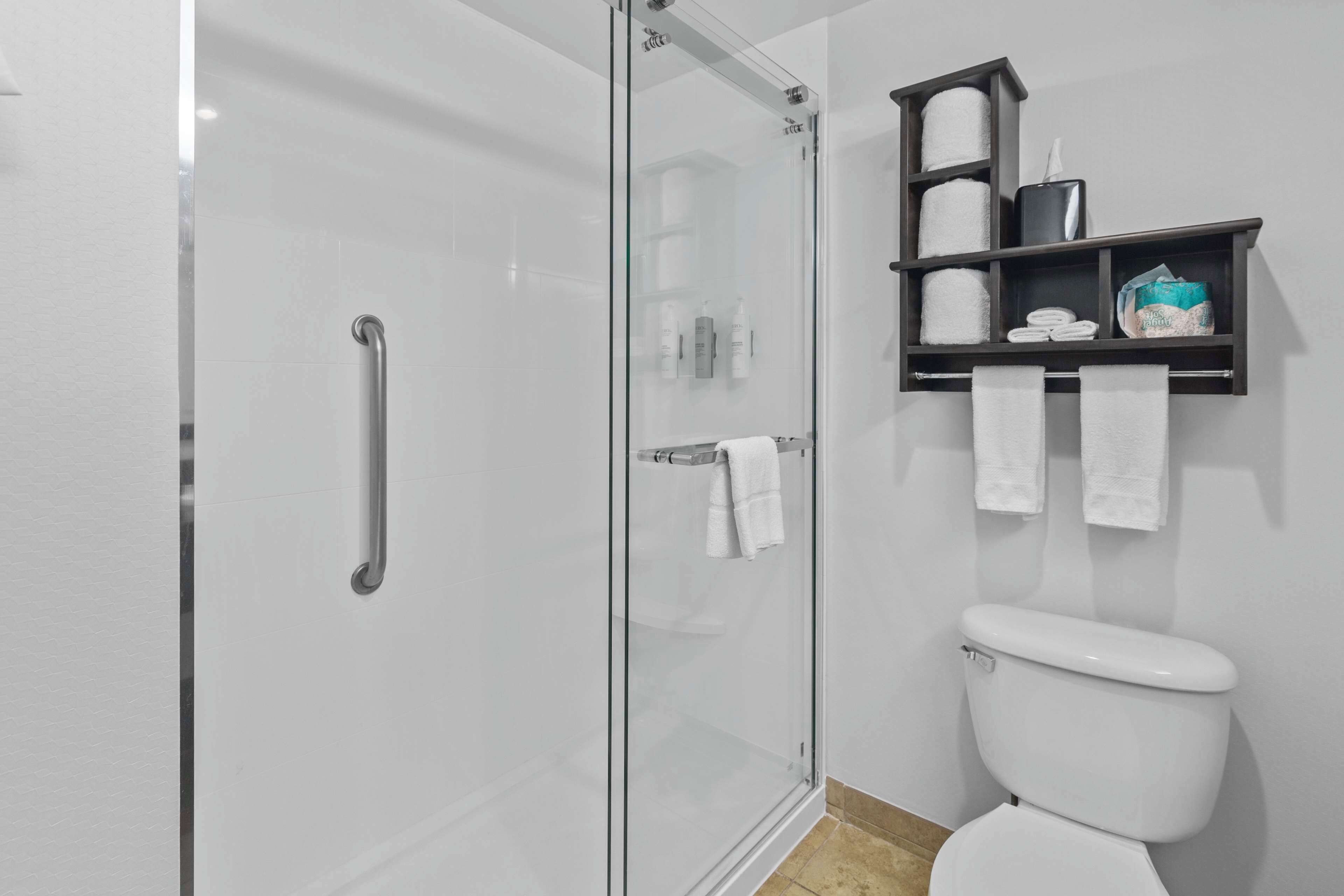 A modern bathroom with a glass-enclosed shower, a white toilet, and a shelf with toiletries.