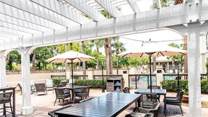 An outdoor patio area with tables and chairs, umbrellas, and a pool in the background. - Hampton Inn & Suites Charleston/West Ashley (Charleston)