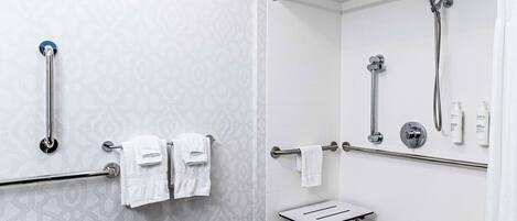 A bathroom with a shower, grab bars, a towel rack, and a small table.