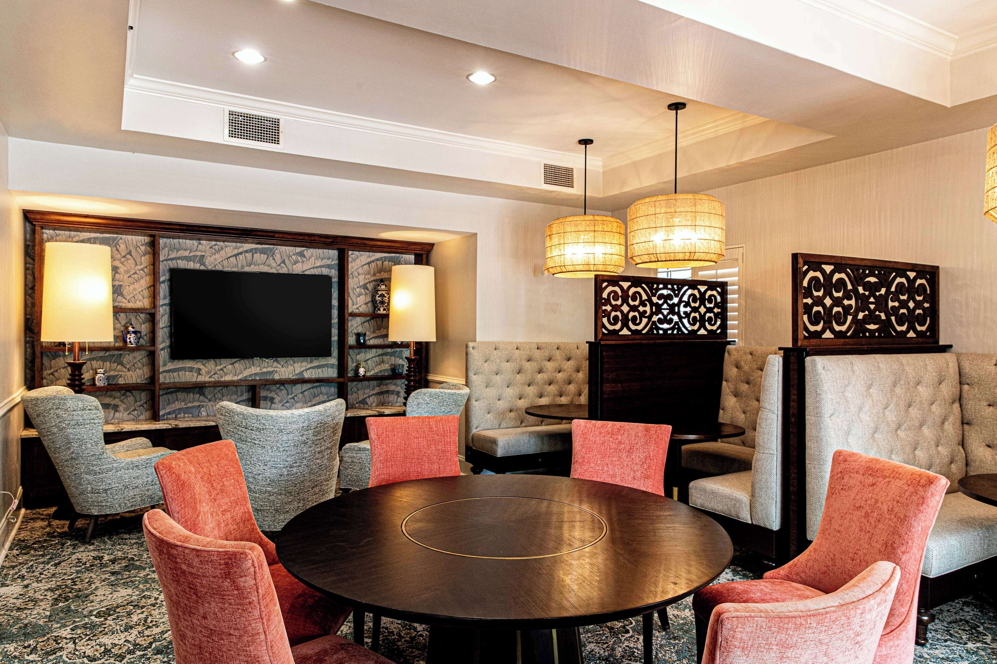 Une chambre d’hôtel dotée d’un grand téléviseur à écran plat, d’une table de salle à manger ronde et de plusieurs fauteuils rembourrés.