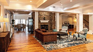 A spacious living room with hardwood flooring, a stone fireplace, and a dining area with a glass-top table and chairs. - Hampton Inn & Suites Charleston/West Ashley (Charleston)