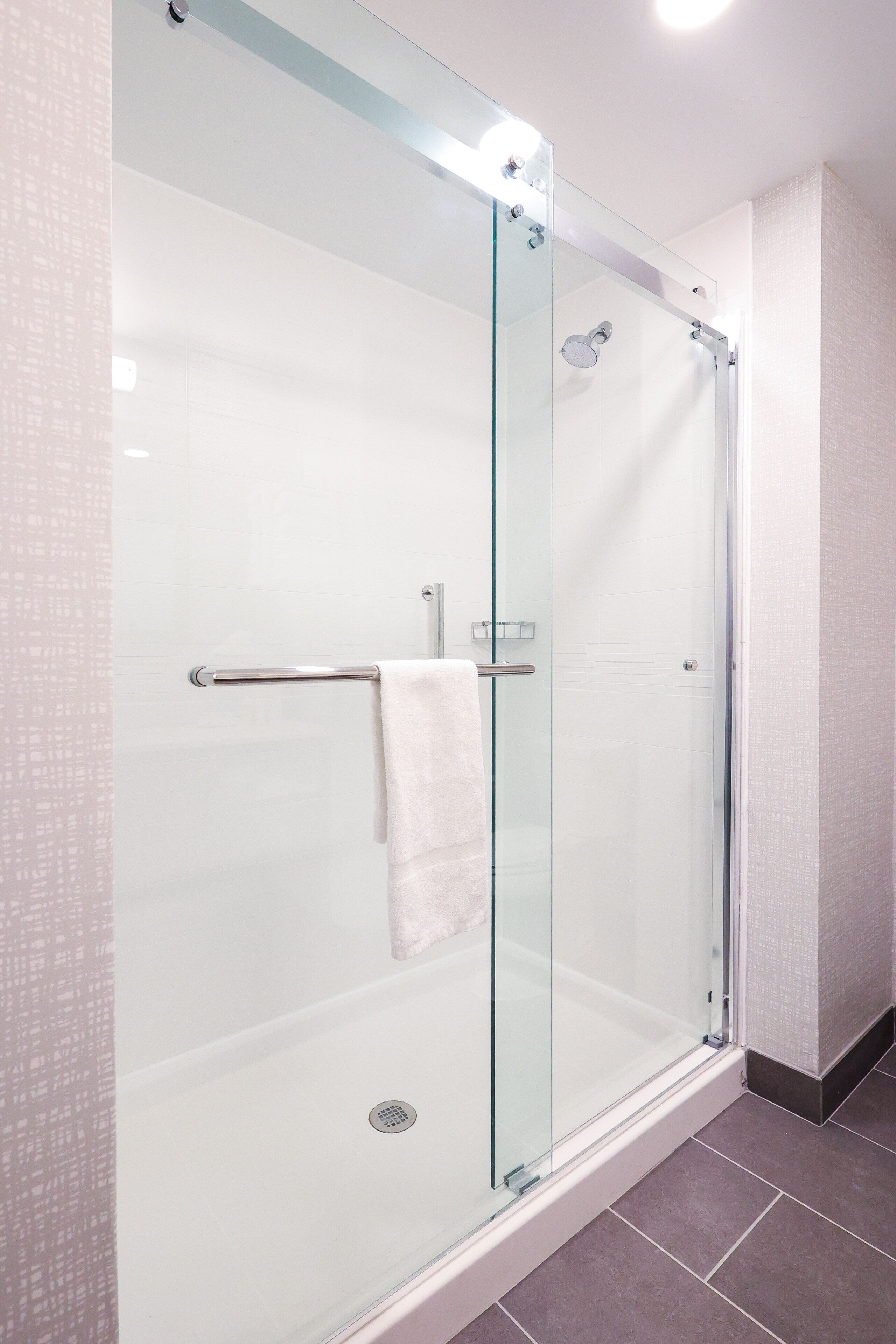 A glass-enclosed shower with a white towel hanging on a metal bar.