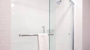 A glass-enclosed shower with a white towel hanging on a metal bar.
