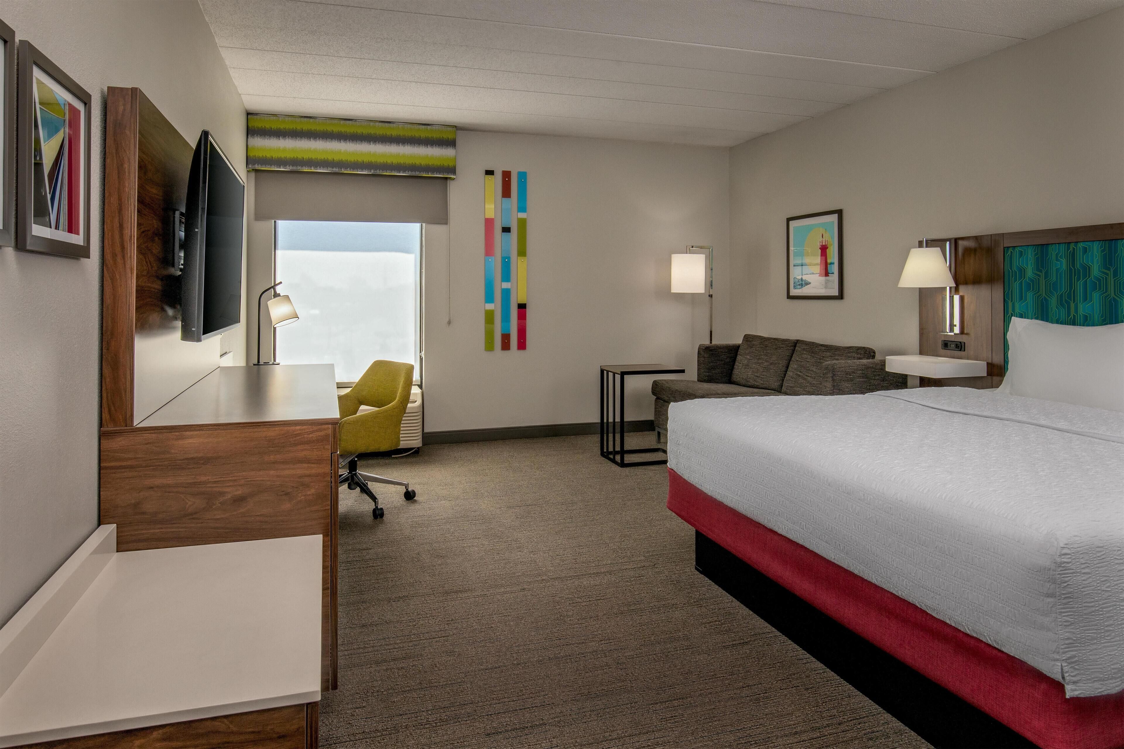 A hotel room with a bed, a desk, a chair, a TV, and a window.
