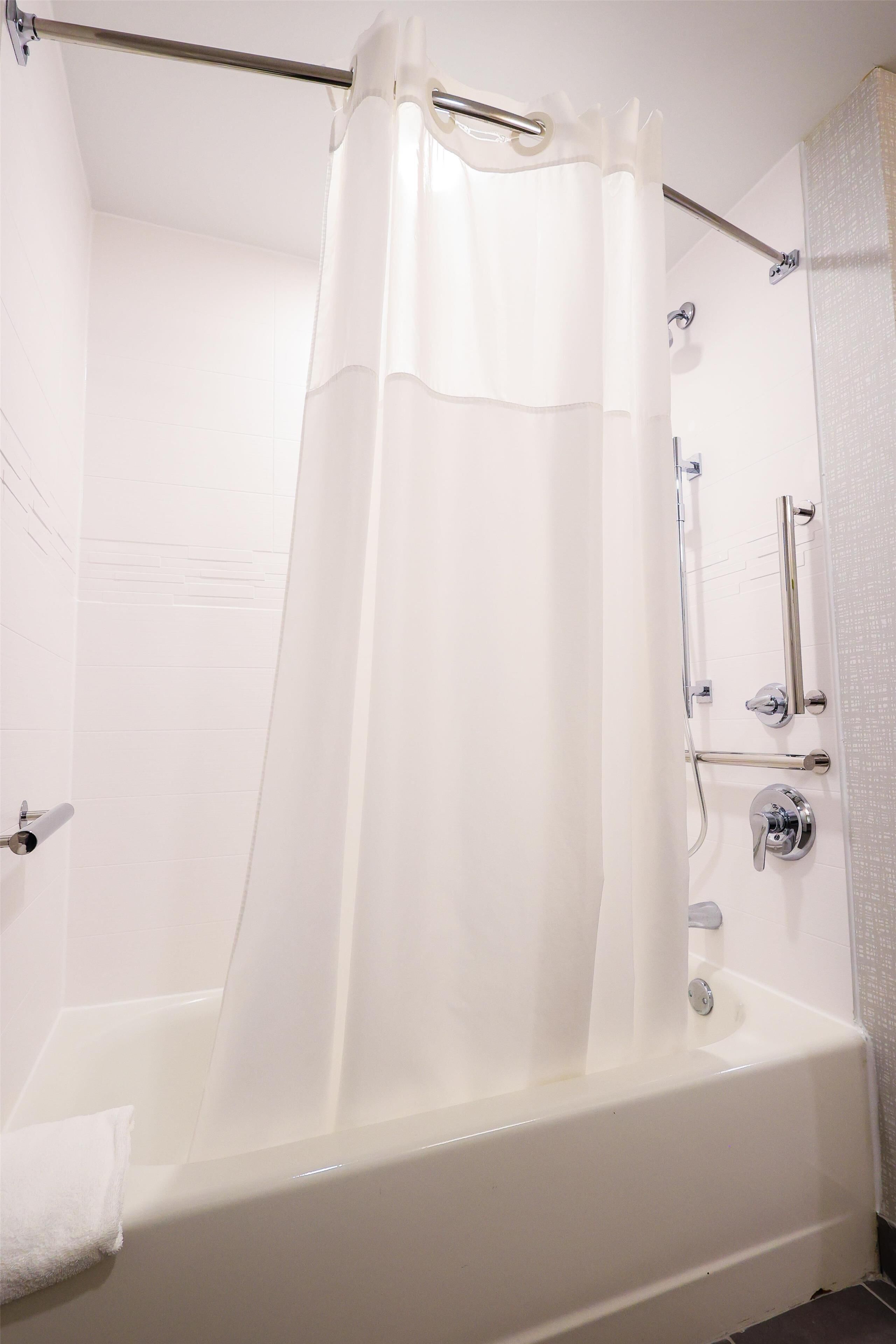 A white bathtub with a shower curtain, a grab bar, and a towel rack.