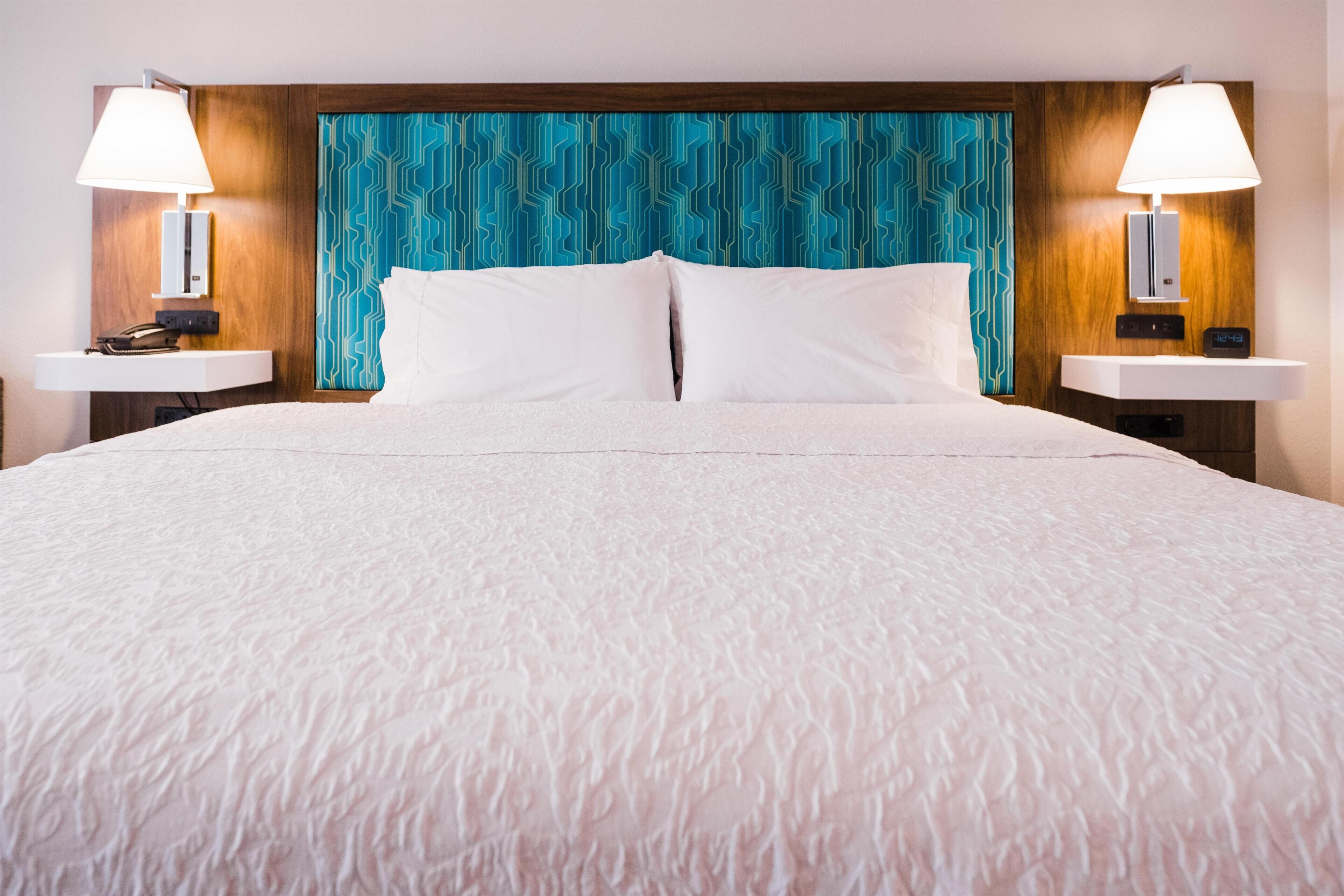 Una habitación de hotel con una cama grande, dos mesitas de noche con lámparas, un cabecero de madera y una pared con diseño.