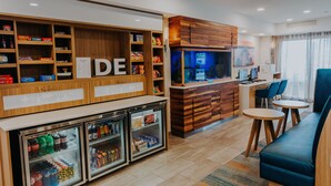 Un hall de hotel con mostrador de recepción, máquinas expendedoras, un acuario, zona de estar y un refrigerador con bebidas.