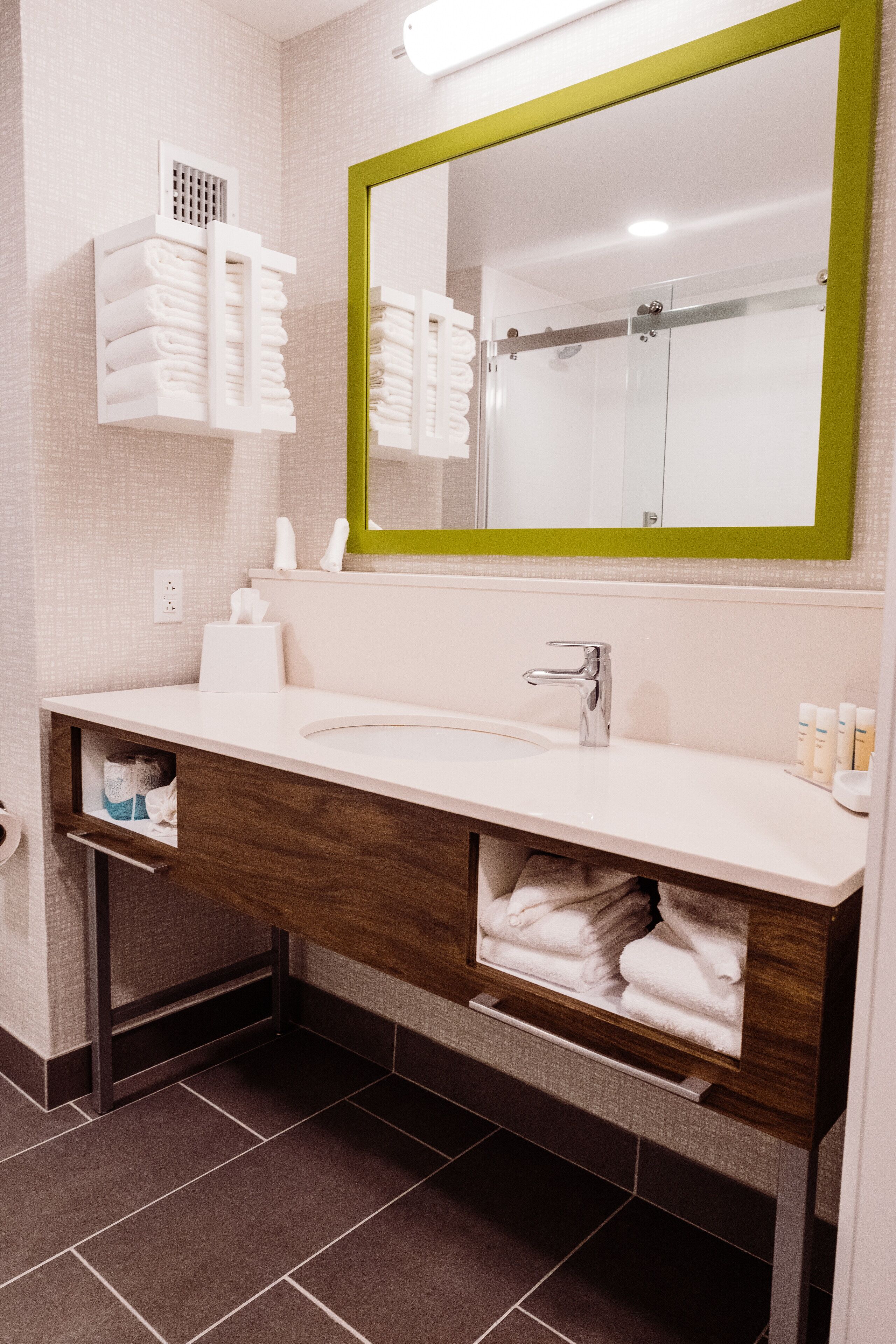 Un baño moderno con un lavabo blanco, un espejo con marco verde y un perchero sobre el lavabo.