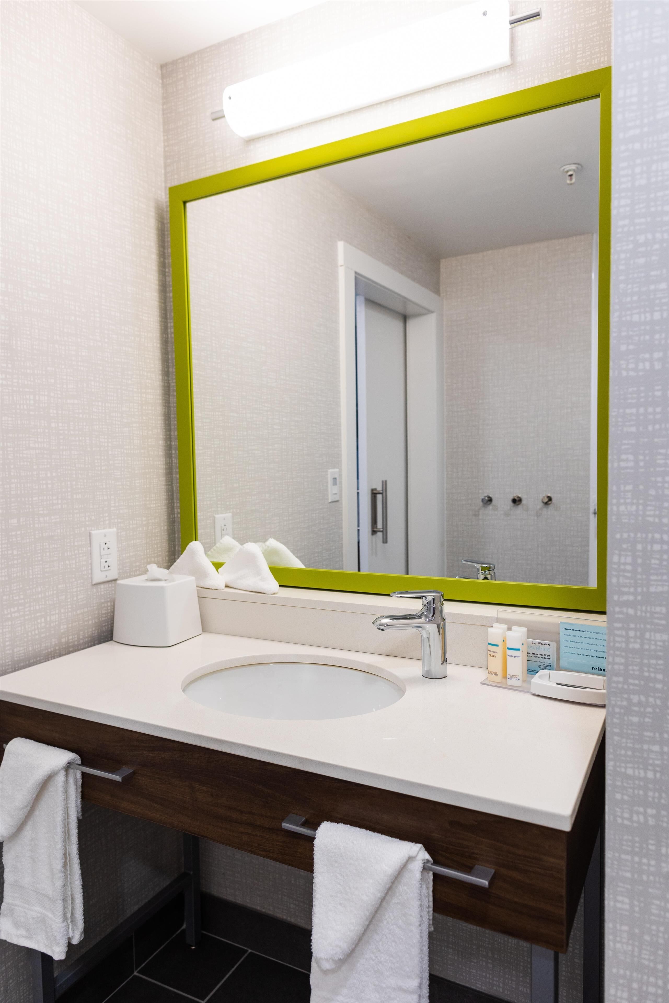 A bathroom with a large mirror, a sink, a towel rack, and a shower visible in the reflection.