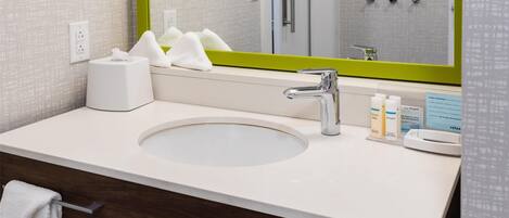 A bathroom with a large mirror, a sink, a towel rack, and a shower visible in the reflection.