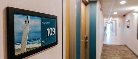 A hallway with a digital welcome sign displaying room number 109 and a beach scene.