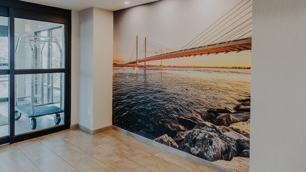 Una habitación con un amplio ventanal, un mural de un puente sobre el agua y un carrito cerca de la ventana.