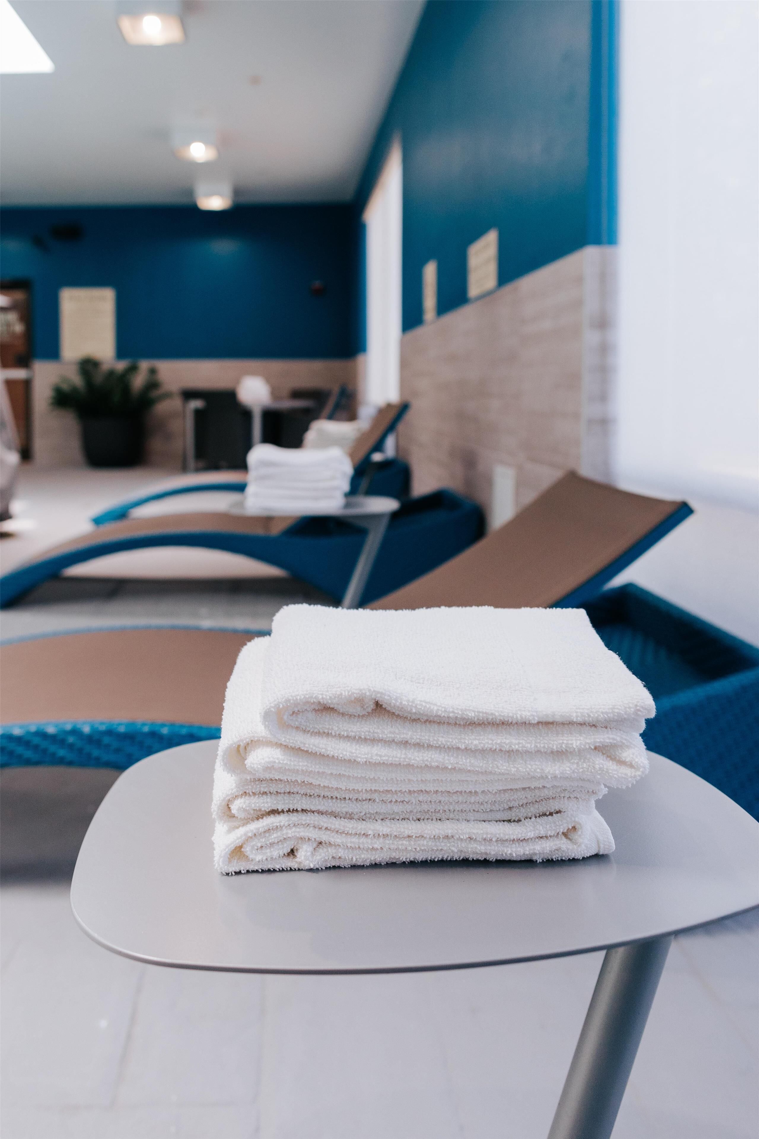 A stack of white towels on a table in a room with a blue wall and a pool area.