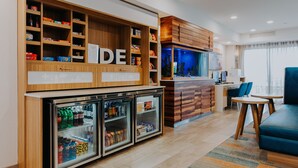 Un vestíbulo de hotel con un mostrador de recepción de madera, un minibar con bebidas y una zona de estar con un sofá y sillas azules.