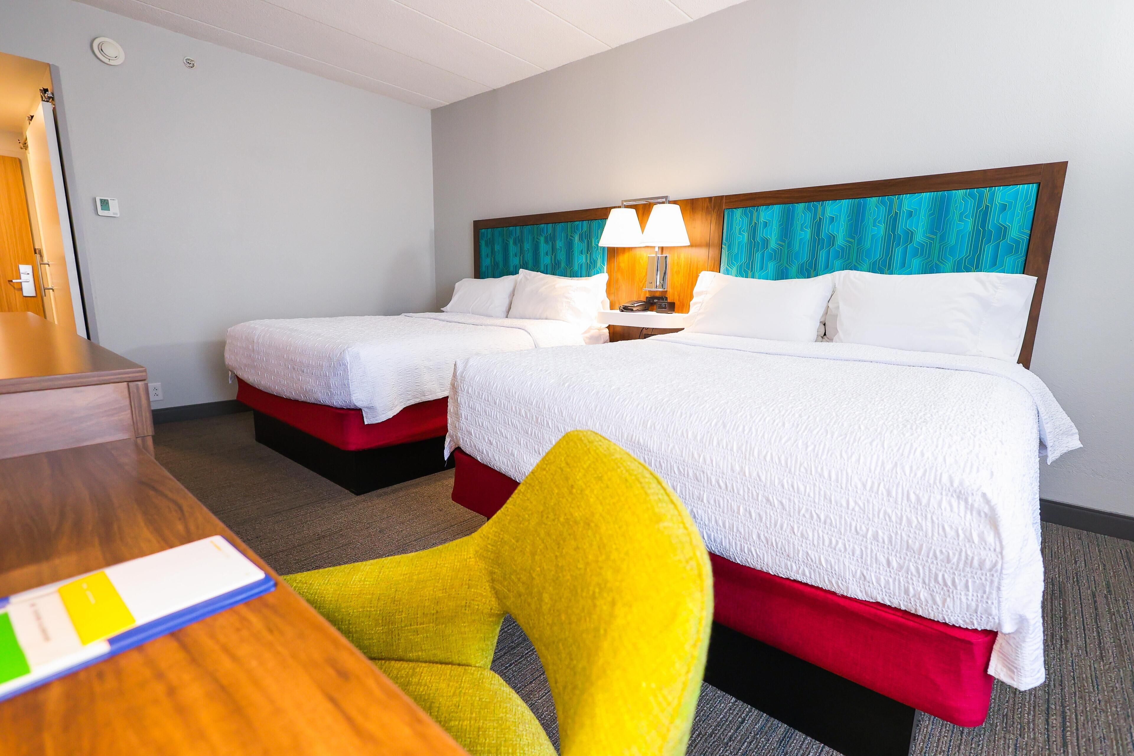 A hotel room with two beds, a desk, and a chair.