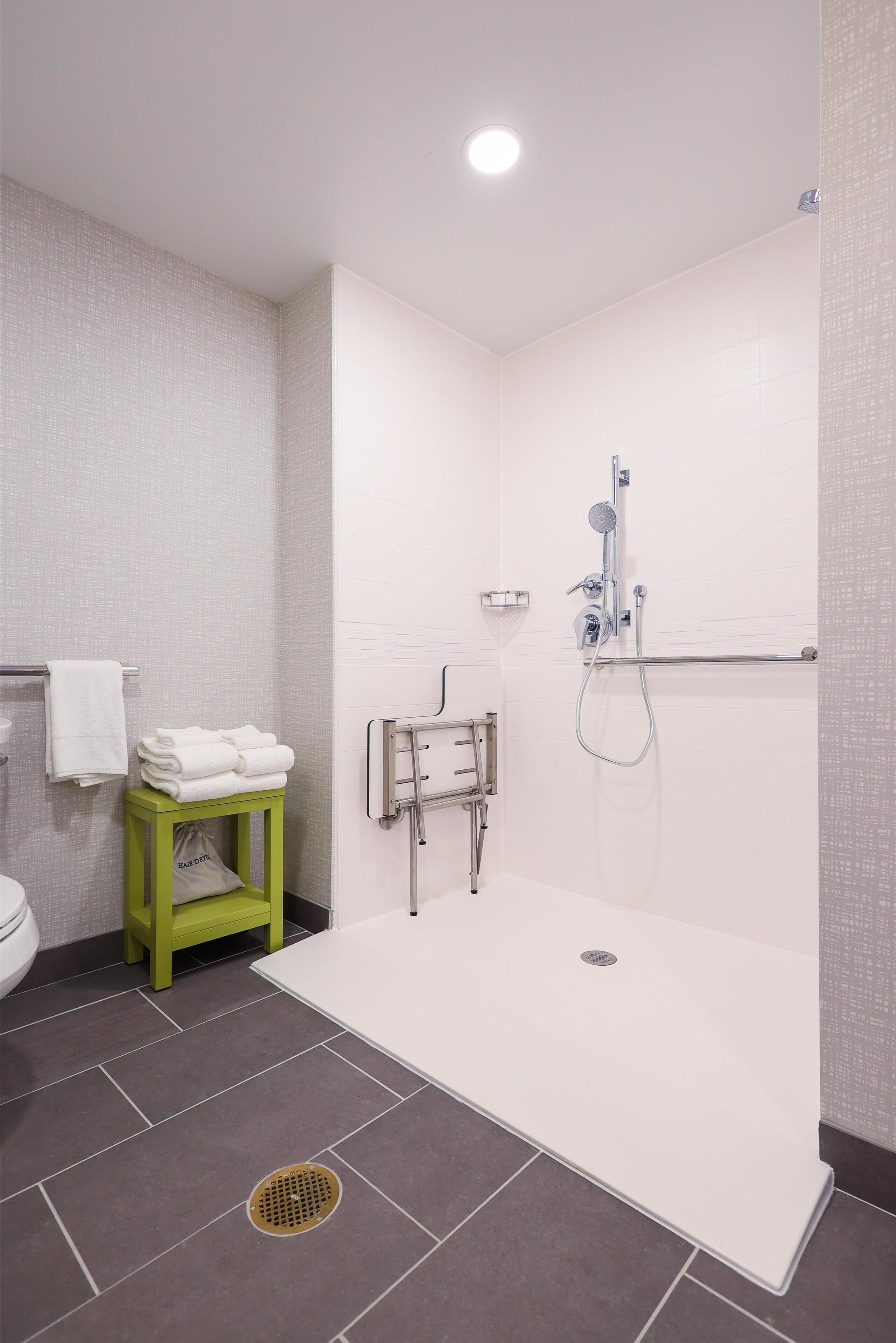 A modern bathroom with a shower, toilet, and a green stool with towels.
