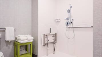 A modern bathroom with a shower, toilet, and a green stool with towels.