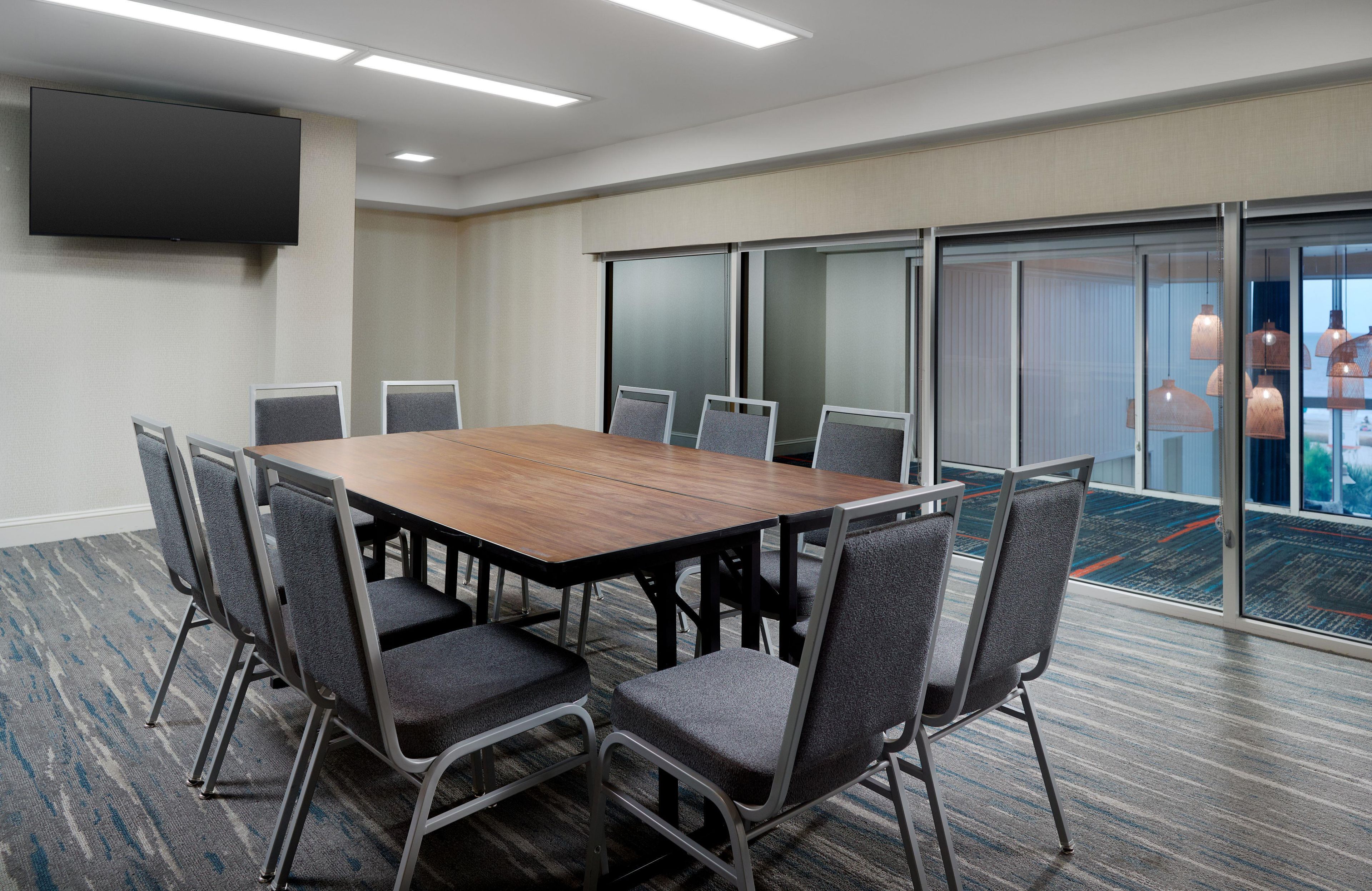 A conference room with a large table, chairs, a flat-screen TV, and a view through glass doors.