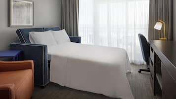 A hotel room with a bed, a desk, a chair, and a large window with curtains.