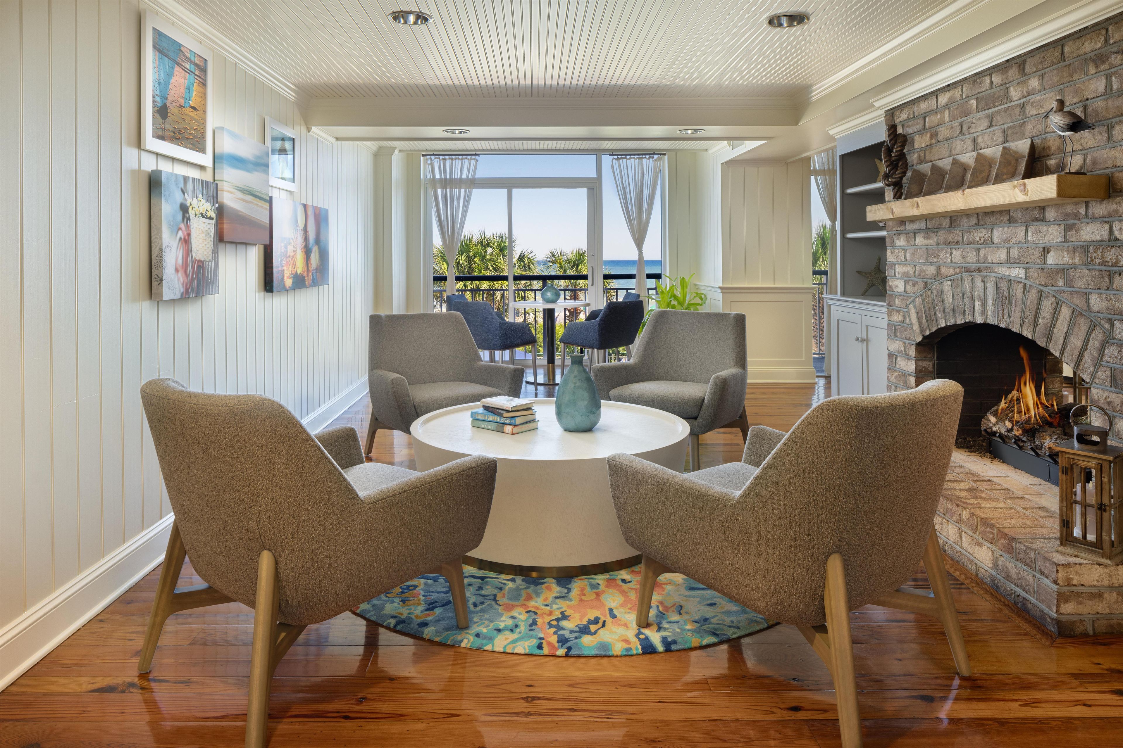 A dining area with a round table, two chairs, a colorful rug, and a fireplace with a brick surround.