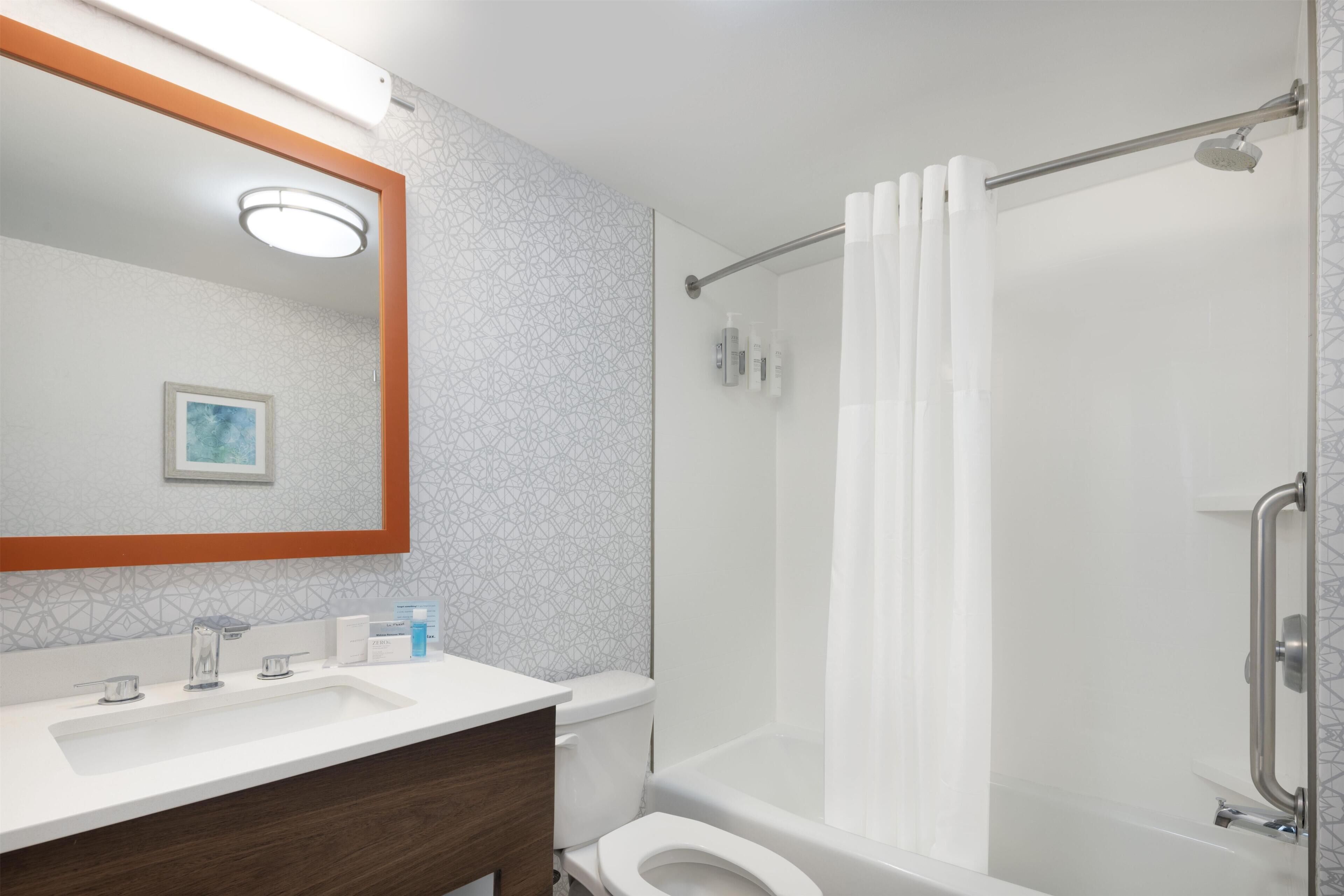 Un baño con ducha, inodoro, lavamanos y espejo.