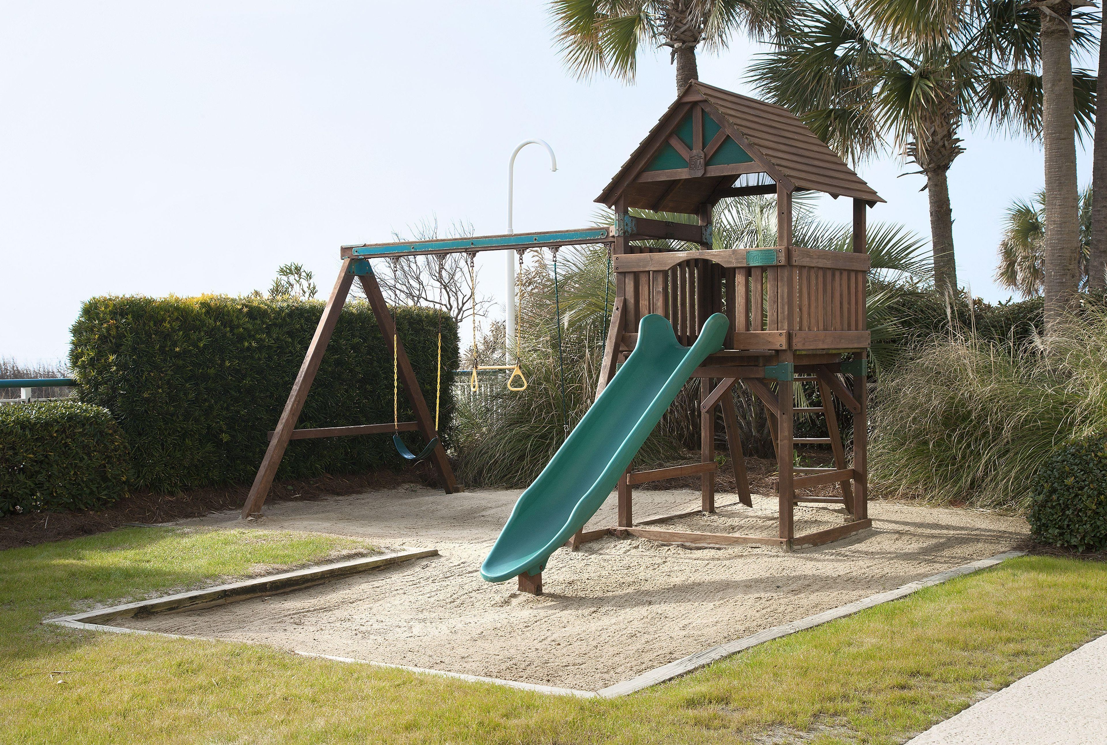 A playground with a slide, swings, and a wooden playhouse.