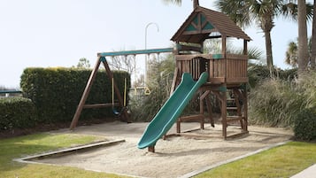 A playground with a slide, swings, and a wooden playhouse.