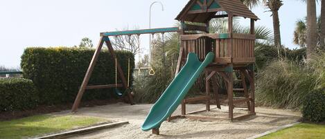 A playground with a slide, swings, and a wooden playhouse.