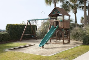 Un parque infantil con un tobogán, columpios y una casita de madera.