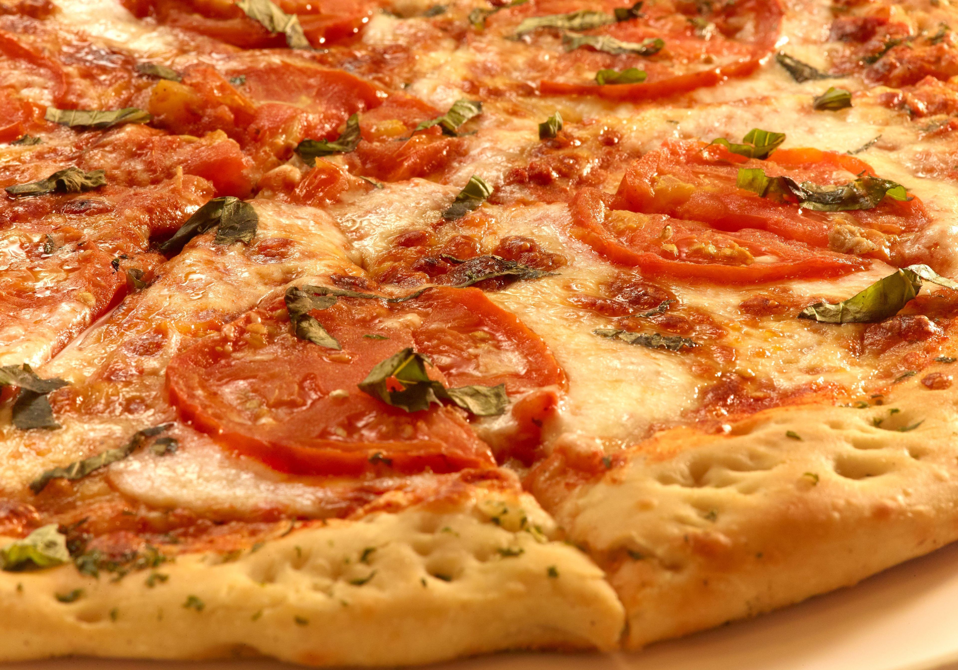 A pizza with tomato slices and basil on a plate.