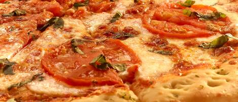A pizza with tomato slices and basil on a plate.