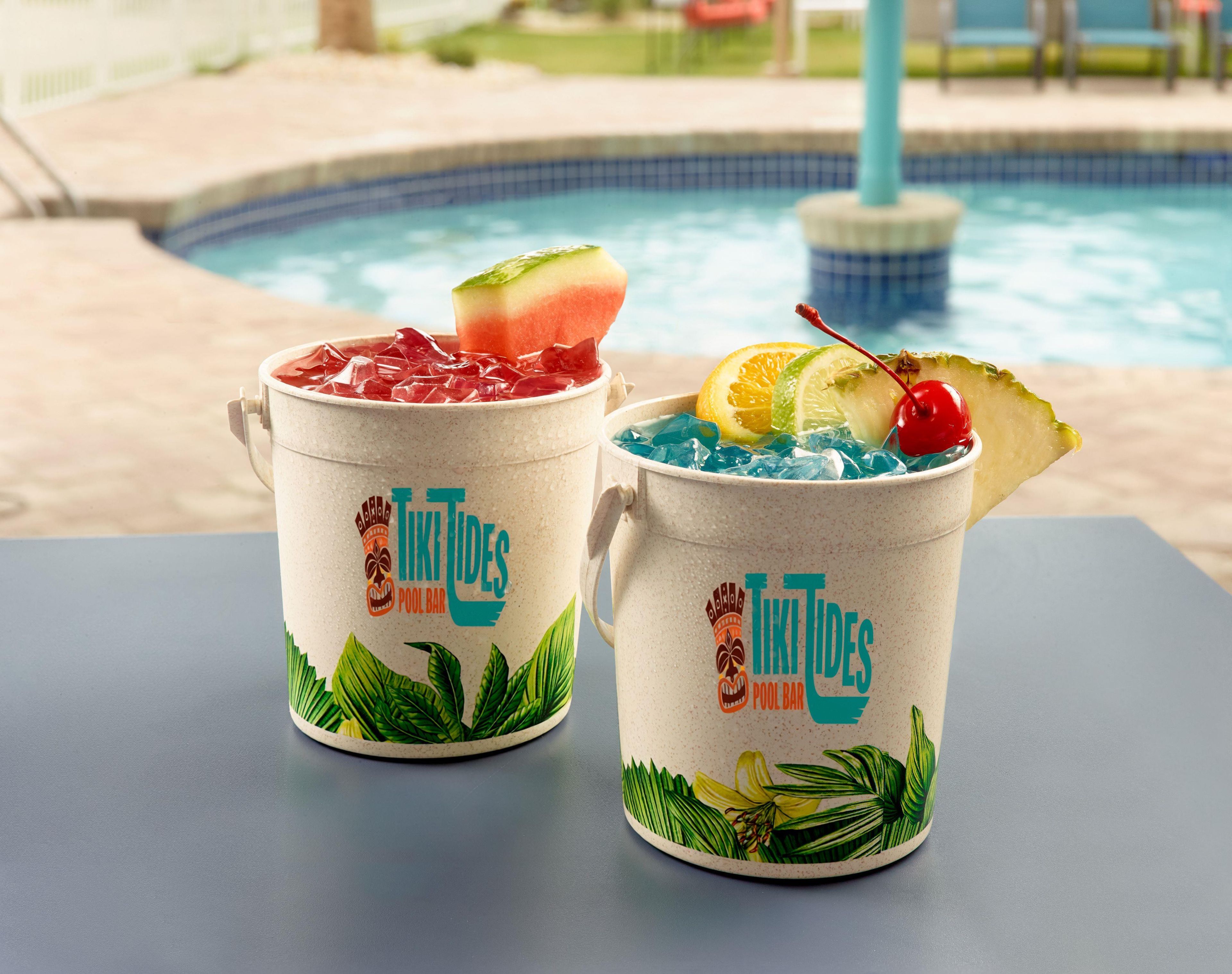Two tiki-themed mugs with tropical designs on a table near a pool.