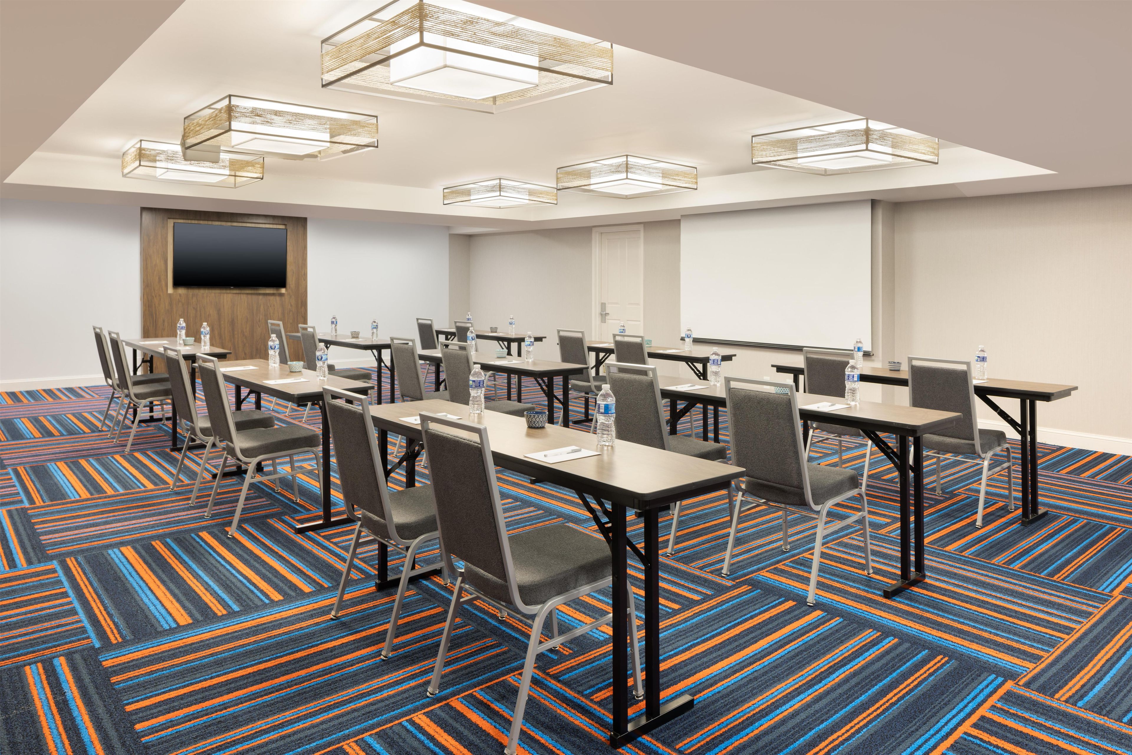 A conference room with tables, chairs, and a large screen.