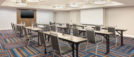A conference room with tables, chairs, and a large screen.