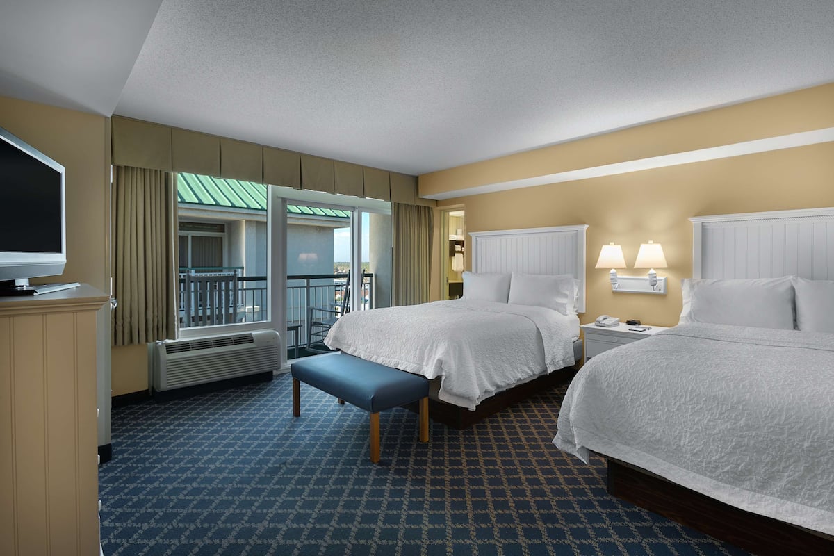 A hotel room with two beds, a television, a desk, and a window with curtains.