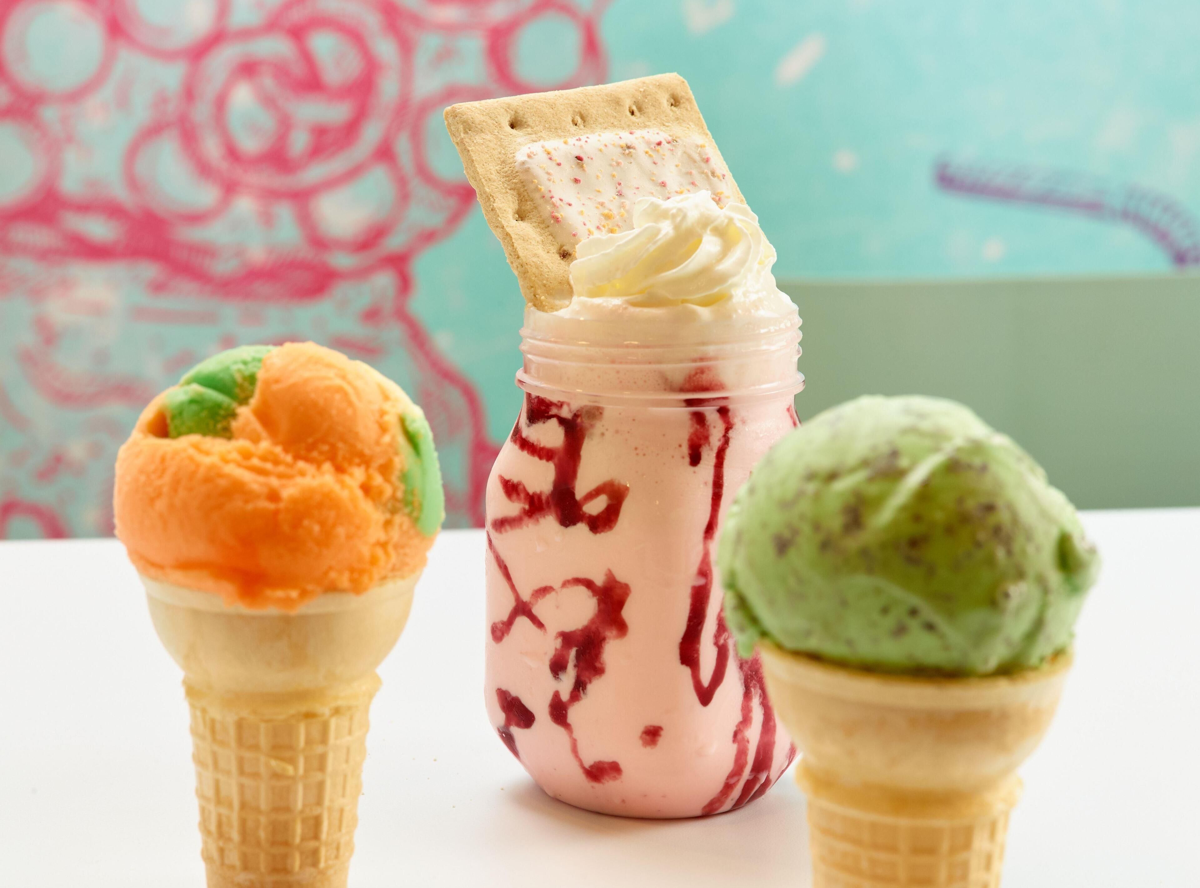 Three ice cream cones with different colors and a jar of pink ice cream with a cookie.