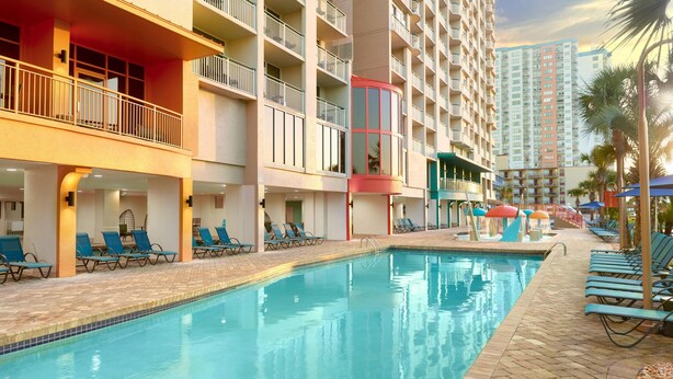 A hotel pool area with multiple levels of balconies, sun loungers, and a clear blue pool.