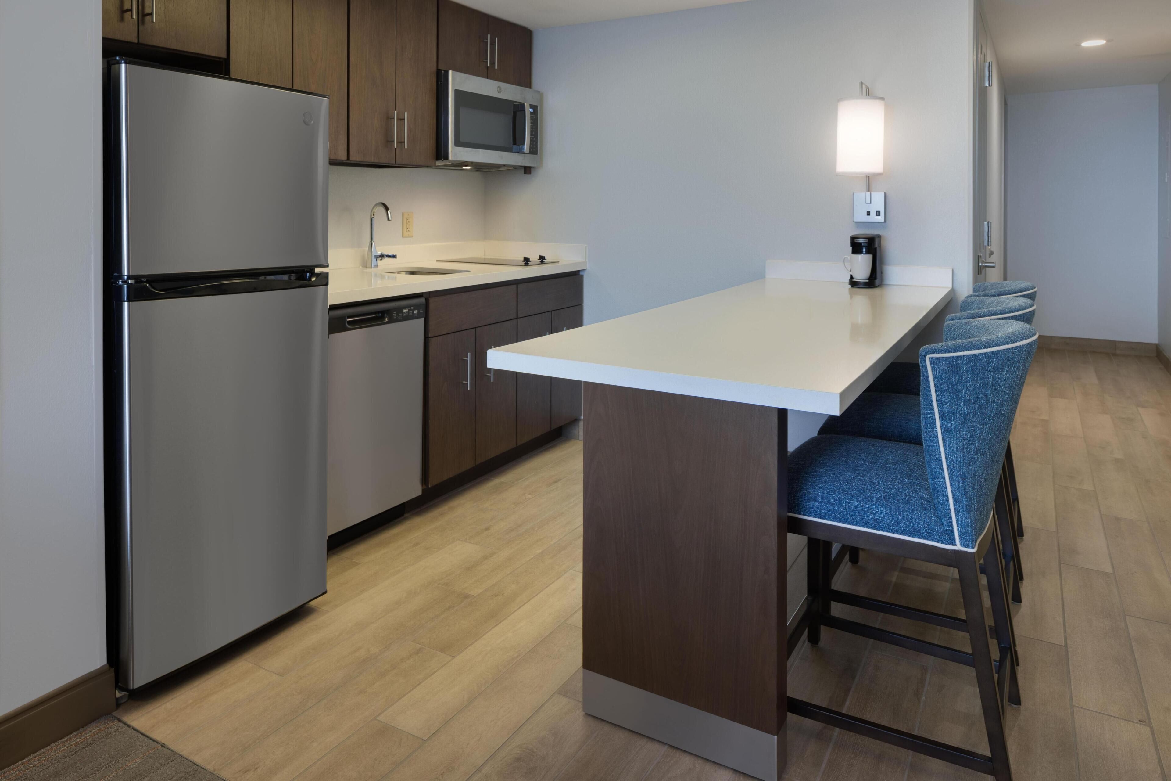 A modern kitchen with a refrigerator, microwave, sink, and bar seating.