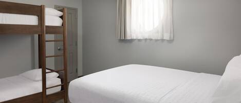 A room with a bunk bed, a single bed, a window with curtains, and a door.