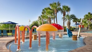 A water play area with colorful mushroom-shaped structures and palm trees in the background.