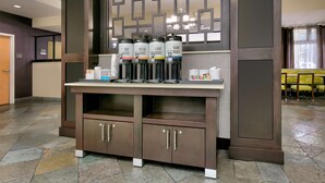 A coffee station with four dispensers labeled 'Hot Water,' 'Decaf Roast,' 'Light Roast,' and 'Dark Roast.' There are cups and a small trash bin on the counter. - Hampton Inn Santa Cruz (Santa Cruz)
