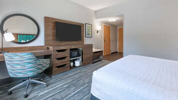 A hotel room with a bed, a desk with a flat-screen TV, a chair, a microwave, and a large mirror.
