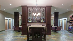 A dining area with a central table and chairs, a decorative wall with geometric patterns, and a ceiling light fixture. - Hampton Inn Santa Cruz (Santa Cruz)