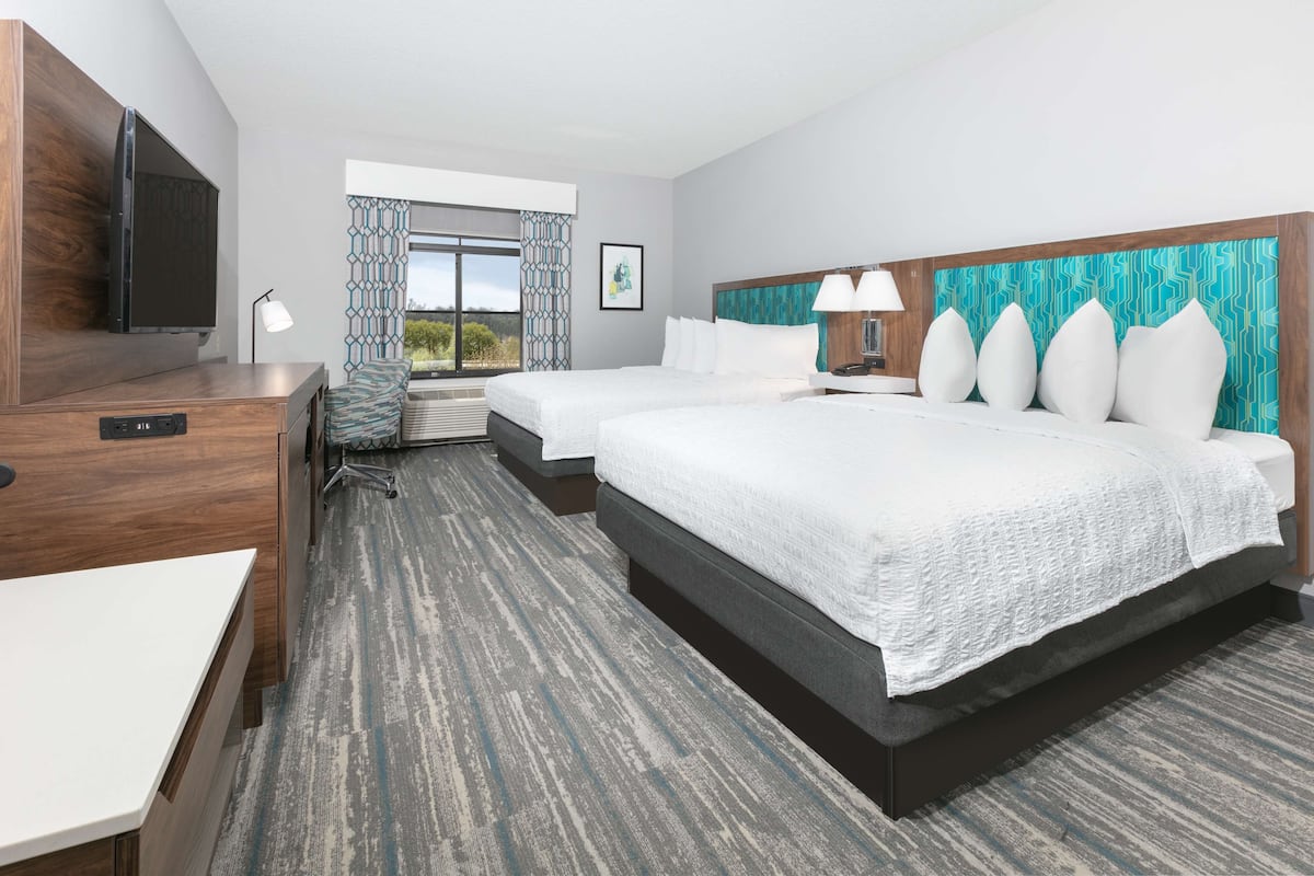 A hotel room with a large bed, a smaller bed, a desk, and a television.