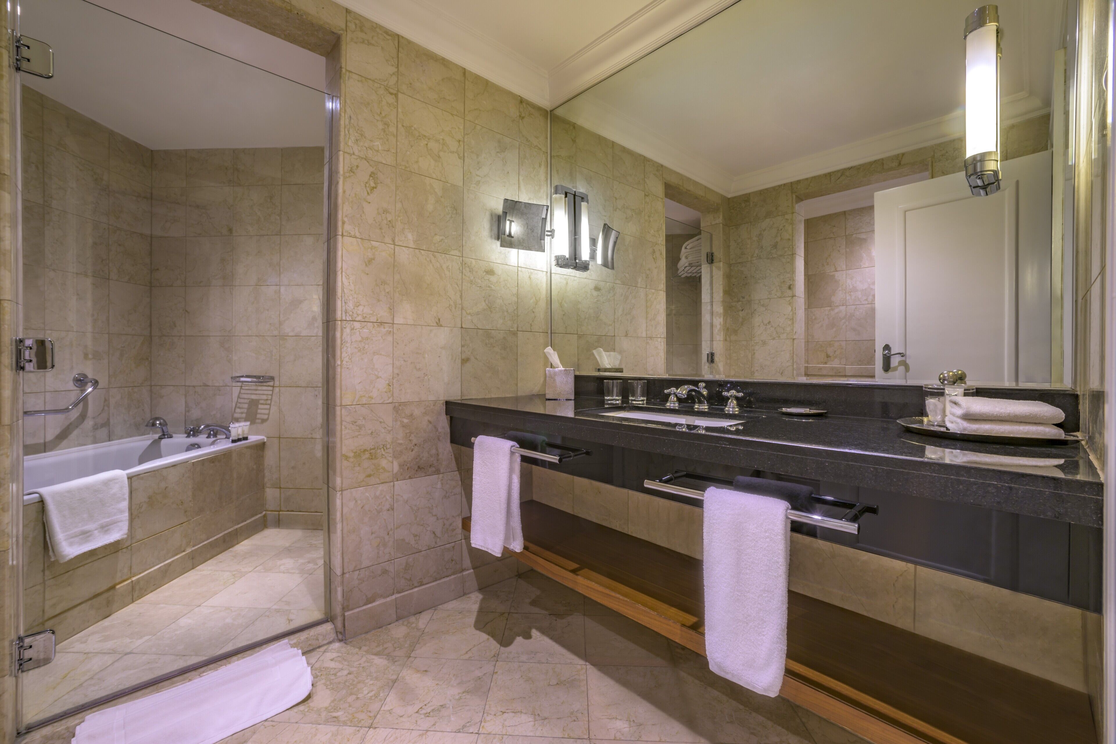 A modern bathroom with a glass-enclosed shower, a large mirror, a black countertop, and a sink.